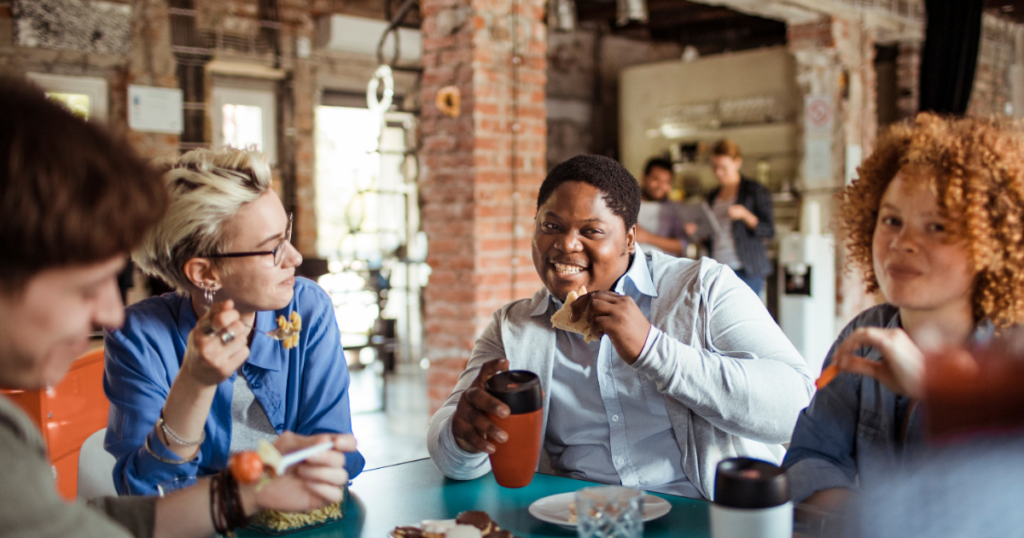 several employees sit together smiling during lunch in a depiction of how to improve company culture