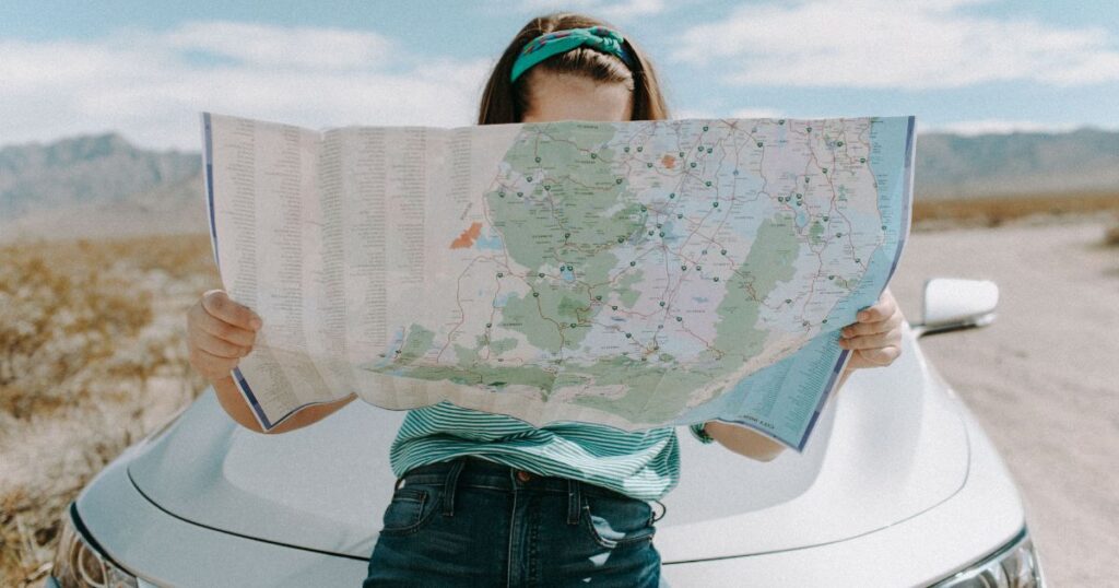 Woman standing in front of a car looking at a street map.