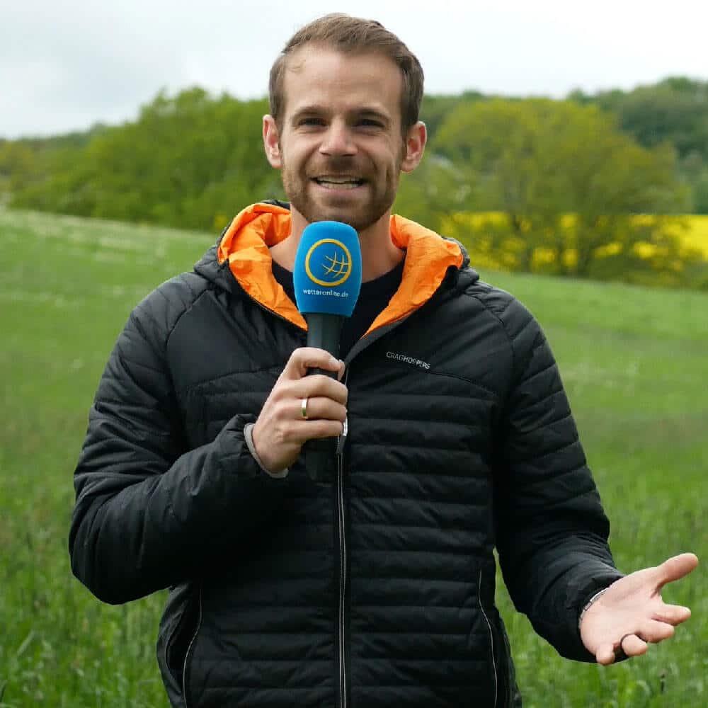 Denis Möller bei einer Moderation für WetterOnline mit Mikrofon auf einer Wiese