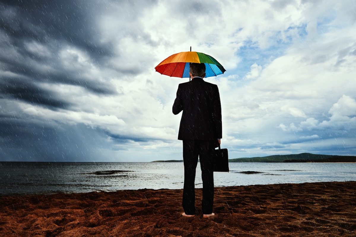 How to use an intranet in a crisis header picture of a man on a beach in a storm with a rainbow umbrella