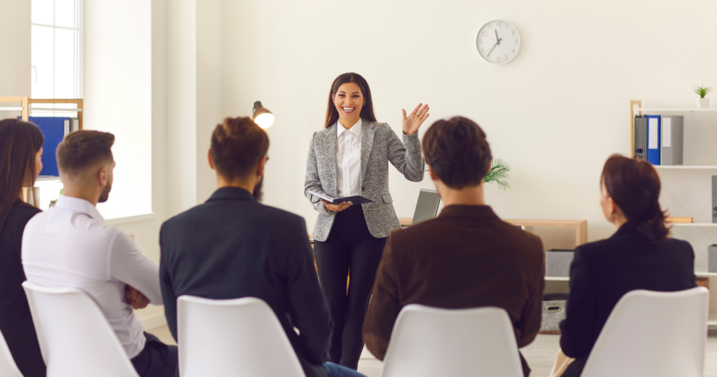 Communicating as a leader image features a woman addressing a room full of professionals