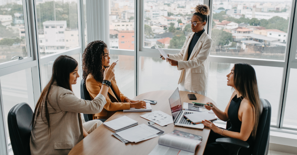 Communicating as a leader image features a woman addressing a room full of professionals in a meeting setting