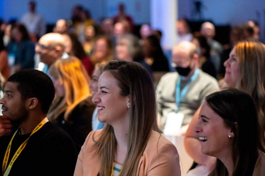 The audience at VOICES 2022 in New York City. A packed room of internal communicators look at the stage, smiling and laughing.