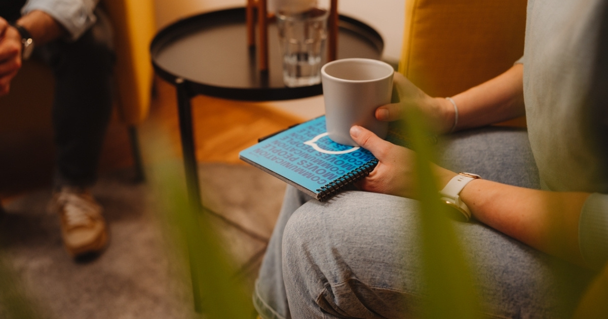 Mitarbeiterin sitzt auf einem Stuhl mit Notizblock und Kaffeetasse und unterhält sich während ihres Onboardings