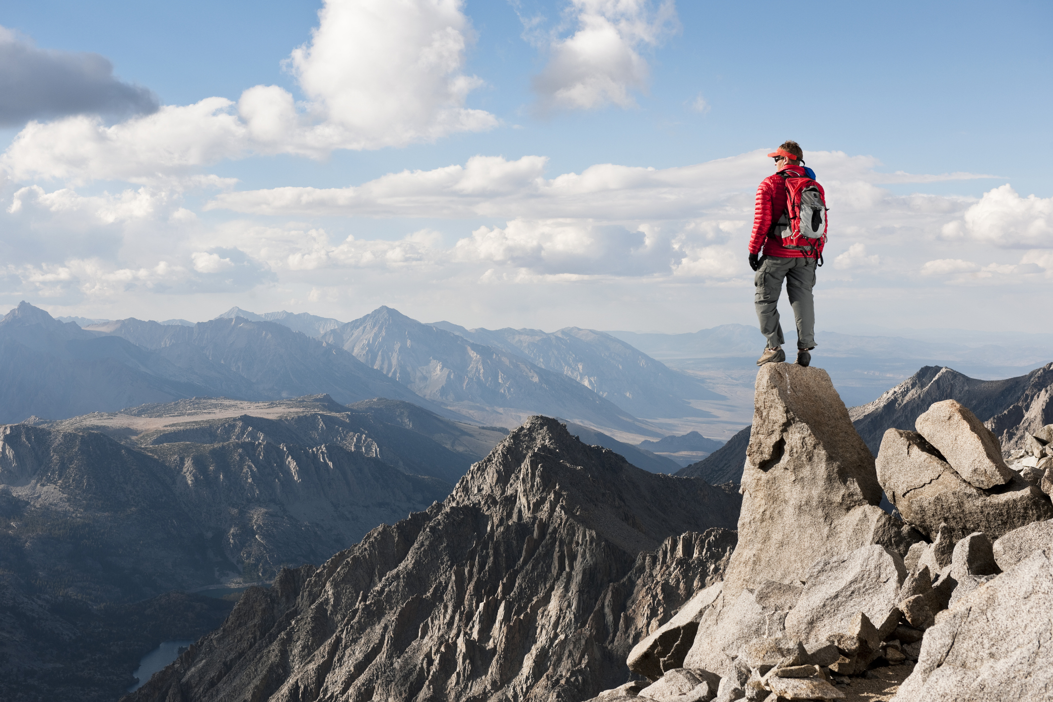 A person in hiking gear stands on top of a mountain and looks out over the summit.