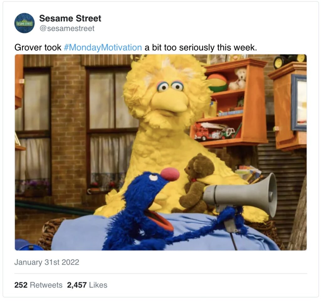 A tweet from the official Sesame Street account. Grover yells into a megaphone while Big Bird looks surprised behind him. The caption reads: "Grover took #MondayMotivation a bit too seriously this week." 