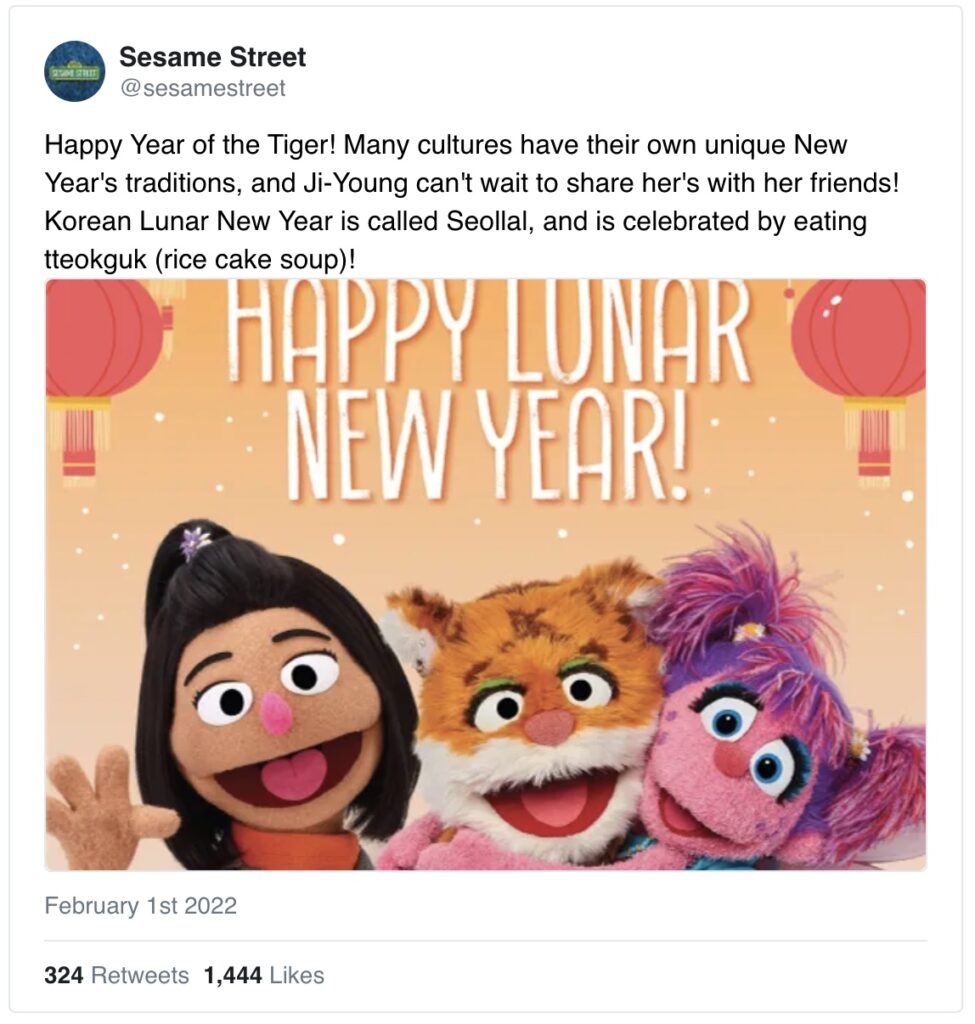 Sesame Street characters embrace a tiger puppet with the words "Happy Lunar New Year!" and lanterns above their heads.