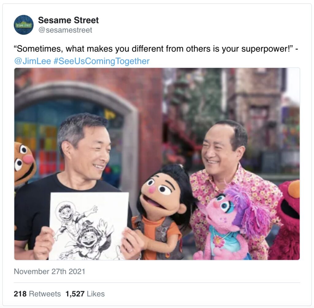 Comic book artist Jim Lee holds up his art while Sesame Street characters look at him in admiration. Everyone is smiling. 